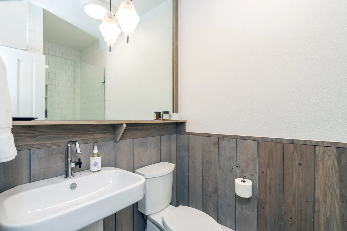 This image captures a remodeled bathroom with a welcoming sink area, well-lit mirror, light fixtures, and attractive wood paneling. The overall atmosphere is inviting and serene, ideal for morning and evening routines.
