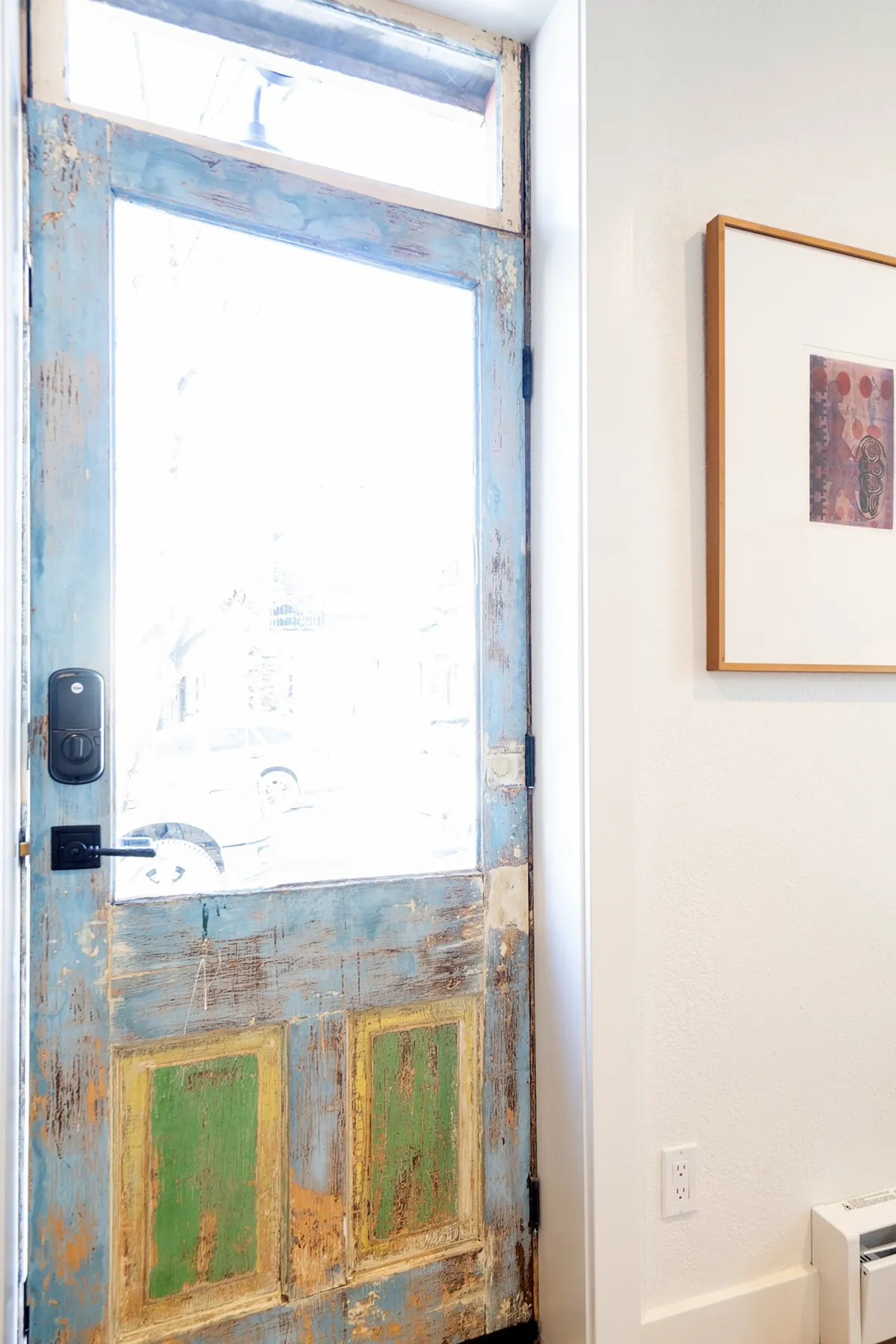 A view of the entryway featuring a rustic door, vibrant color accents, and framed artwork. The scene conveys a sense of arrival and the warmth of being welcomed into a historic home, with unique details that hint at the property's character and heritage.
