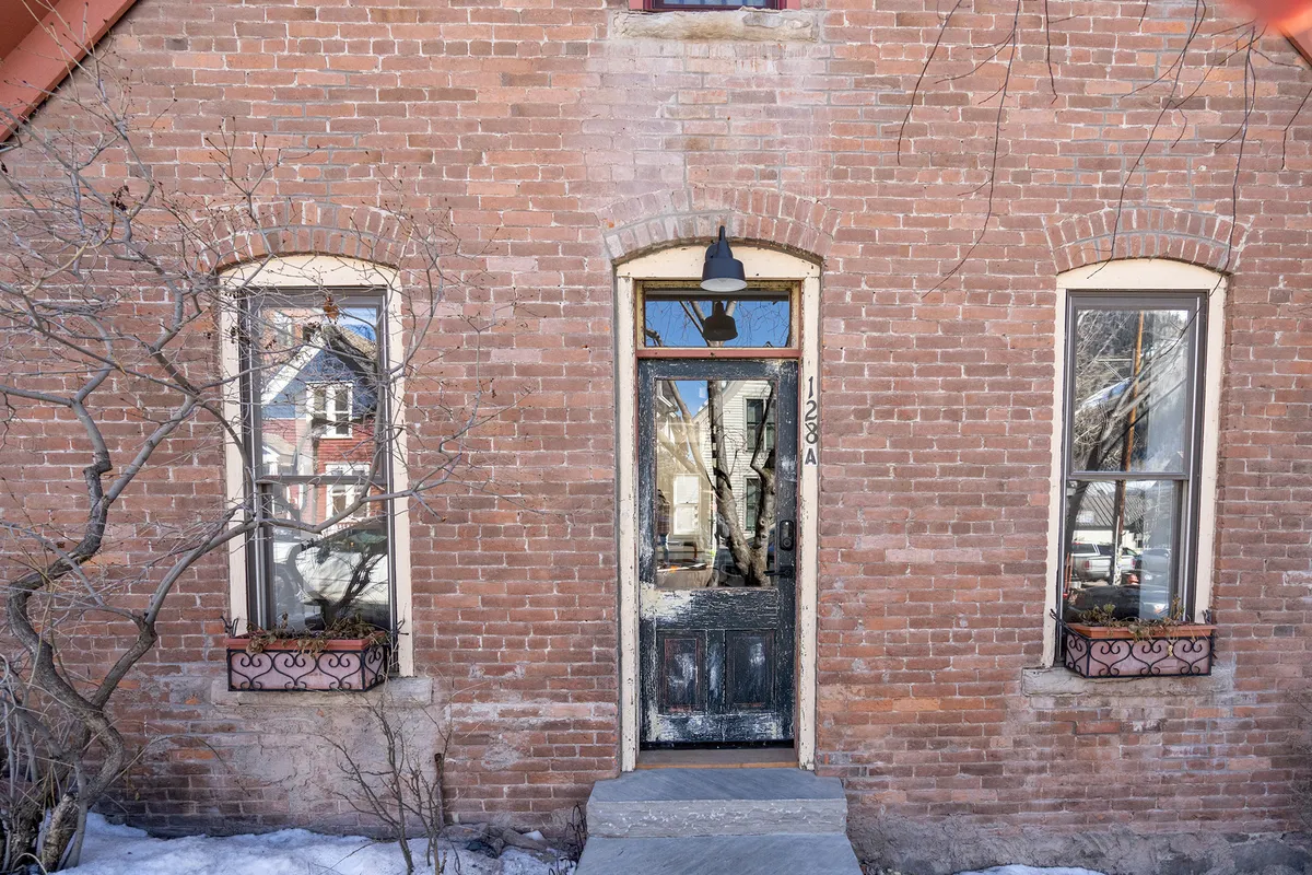 A close-up view of the weathered front door and arched windows set in a brick facade, radiating the warmth and character of a historic Telluride home.