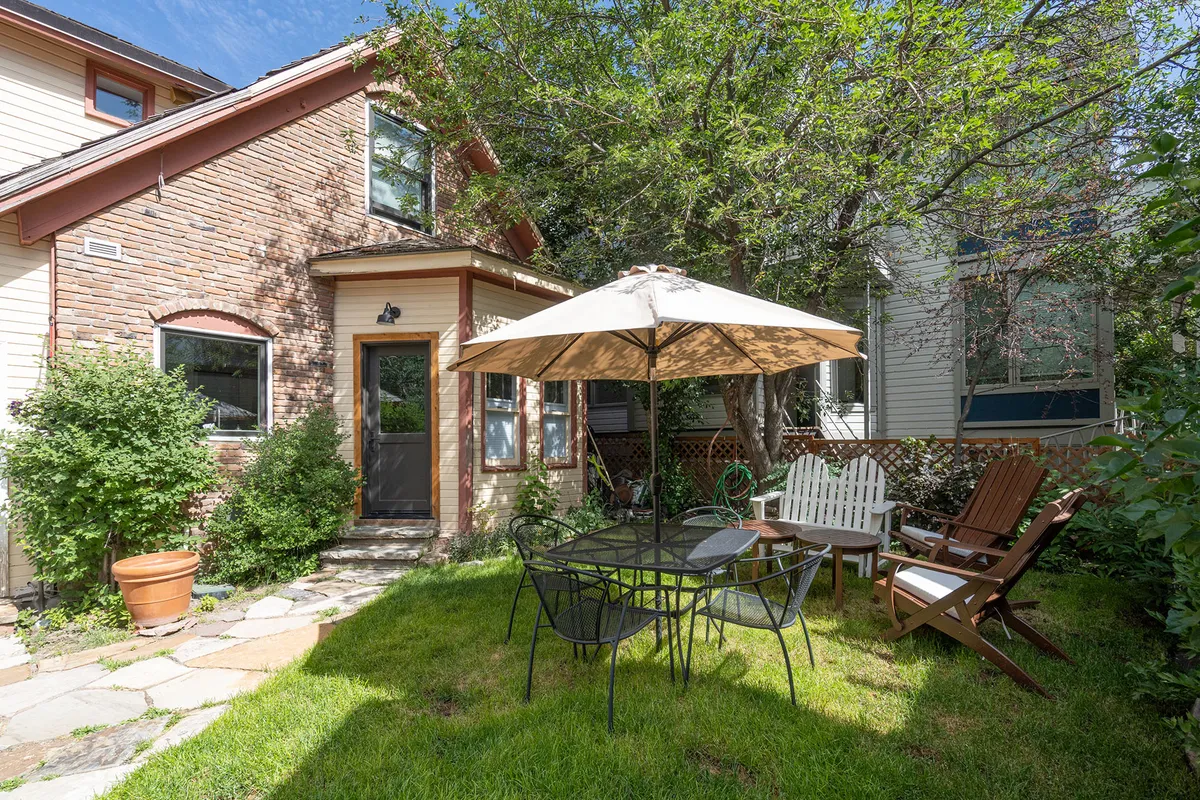 A welcoming outdoor dining area with a large umbrella-covered table and lawn chairs set amidst lush greenery. The setting is ideal for casual gatherings, al fresco meals, and relaxed conversations in an inviting neighborhood environment.